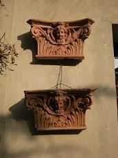 Gruppo di capitelli in cotto toscano, foglie d'acanto racchiuse da volute, testa di putto centrale